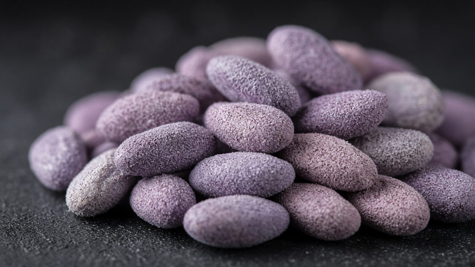 Macro photograph of treated seed in a purple pigmented coating on a dark graphite surface.